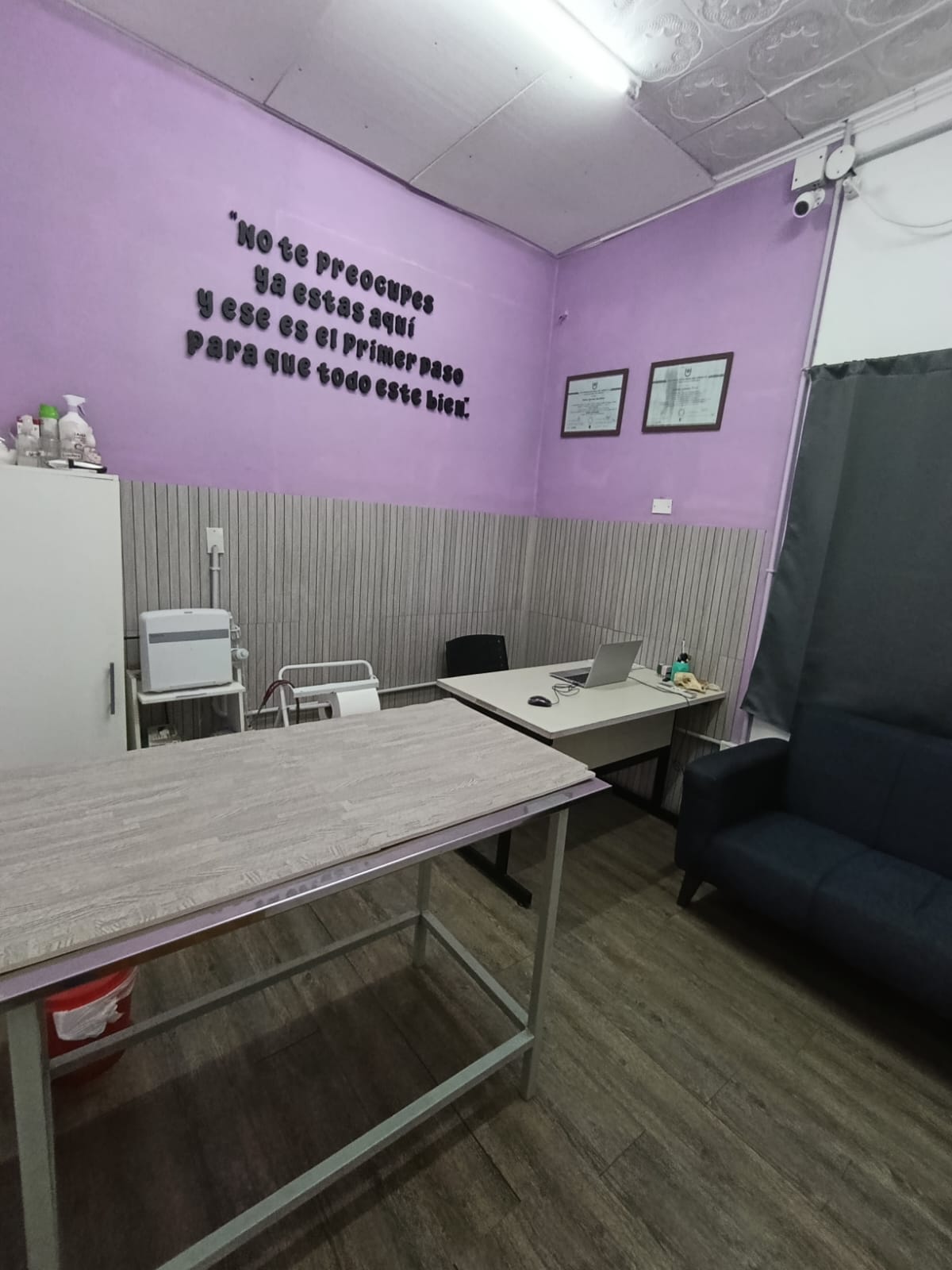 Consultorio de Clivad, con la mesa de examen, el escritorio y los títulos enmarcados en la pared